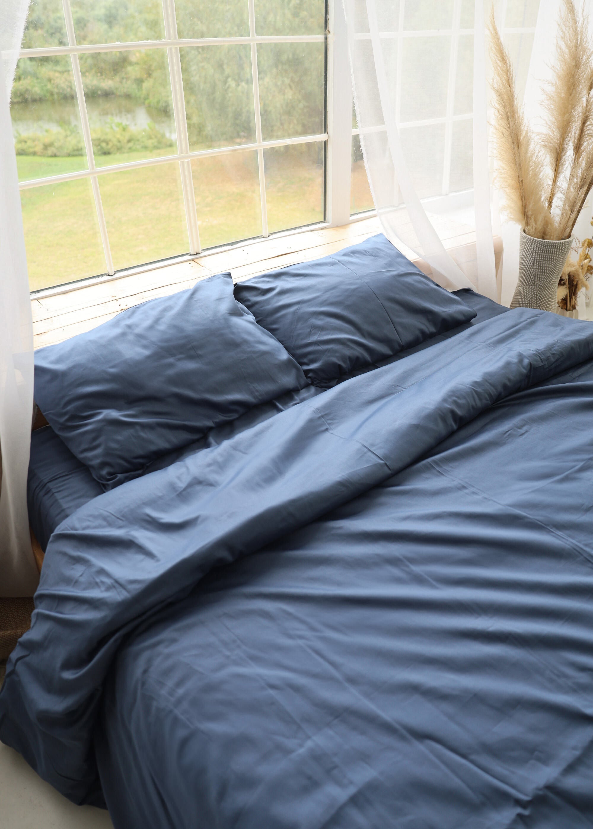 a bed with a blue comforter next to a window