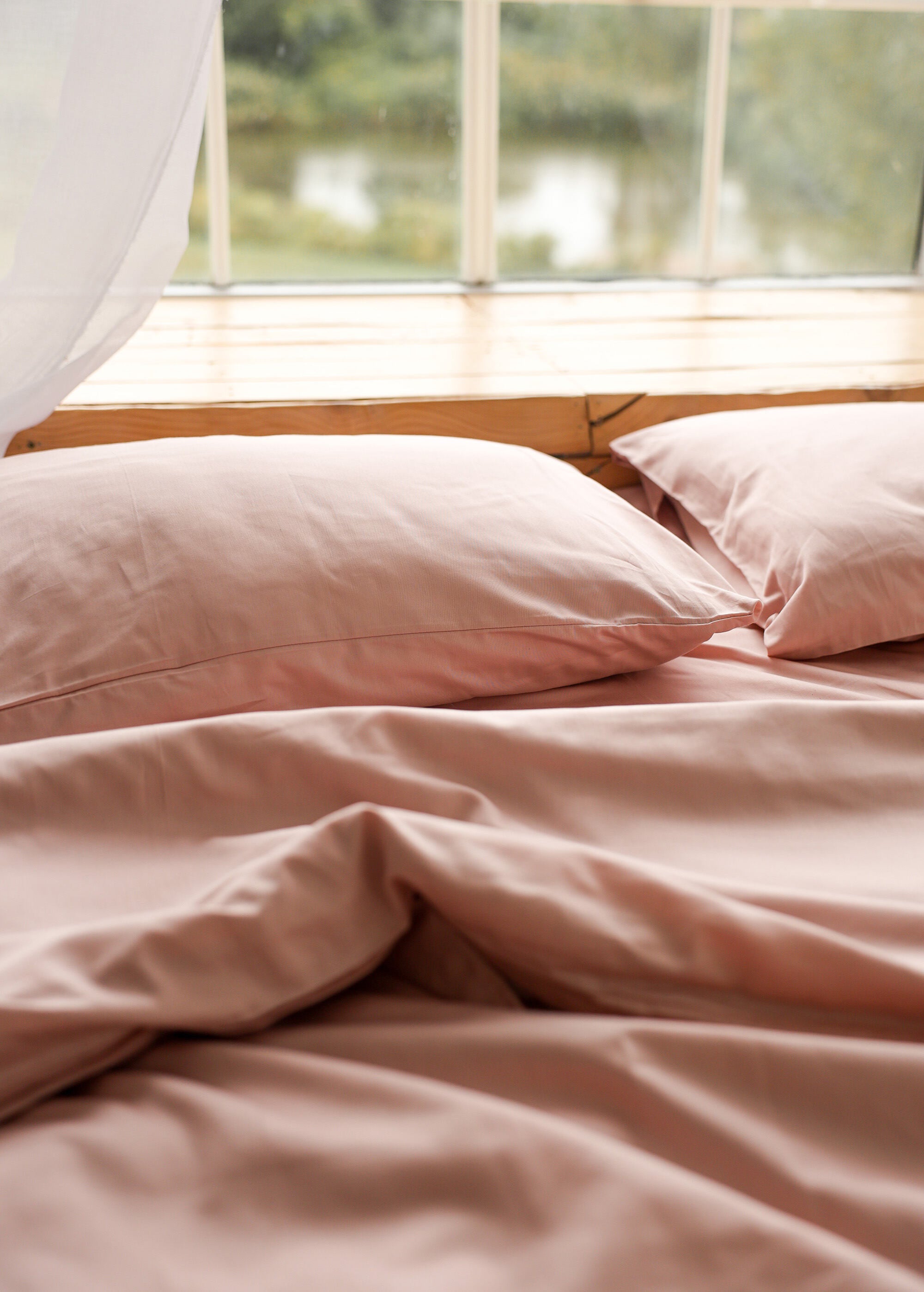 a bed with pink sheets and pillows in front of a window