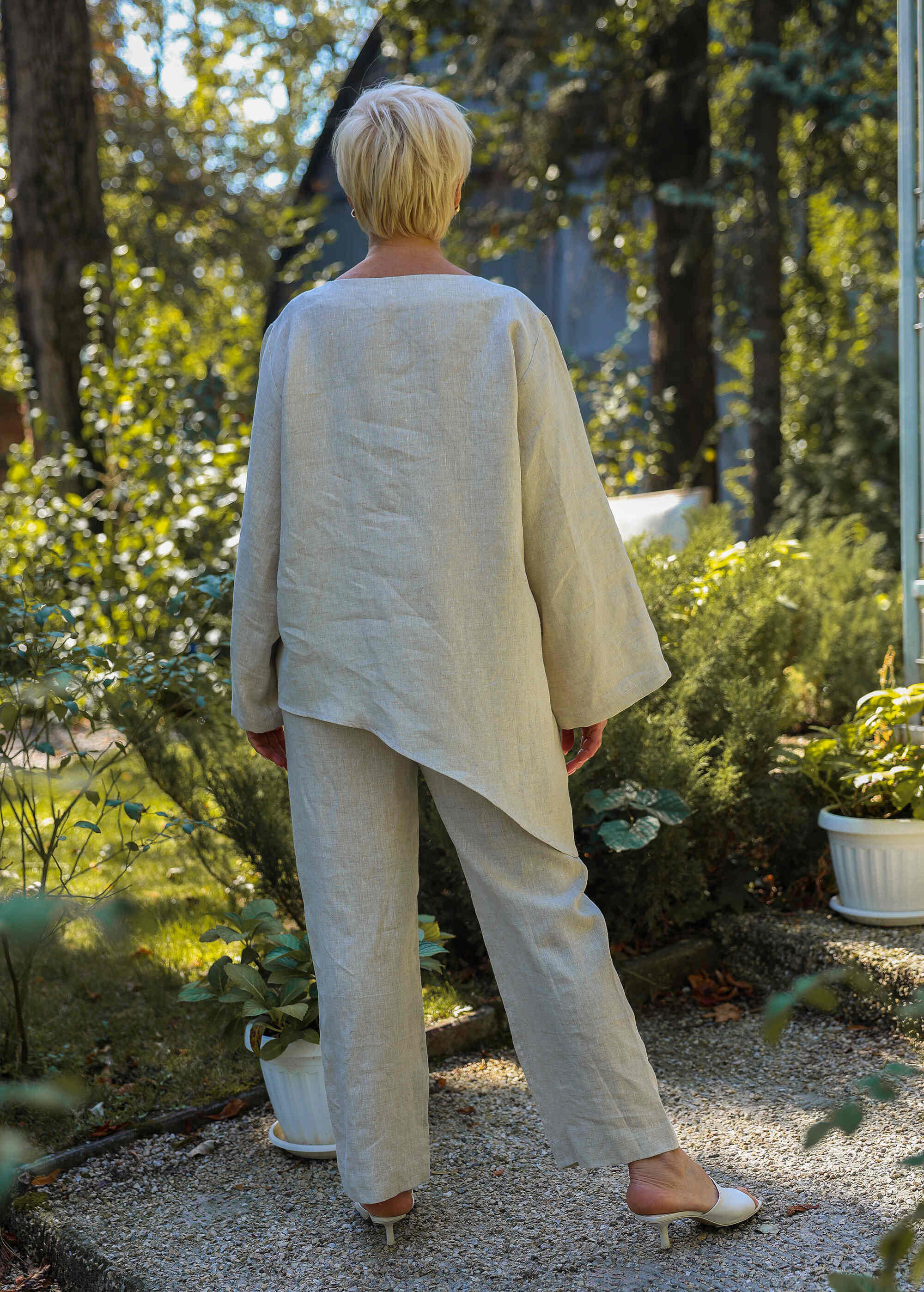 a woman in a white top and pants standing in a garden