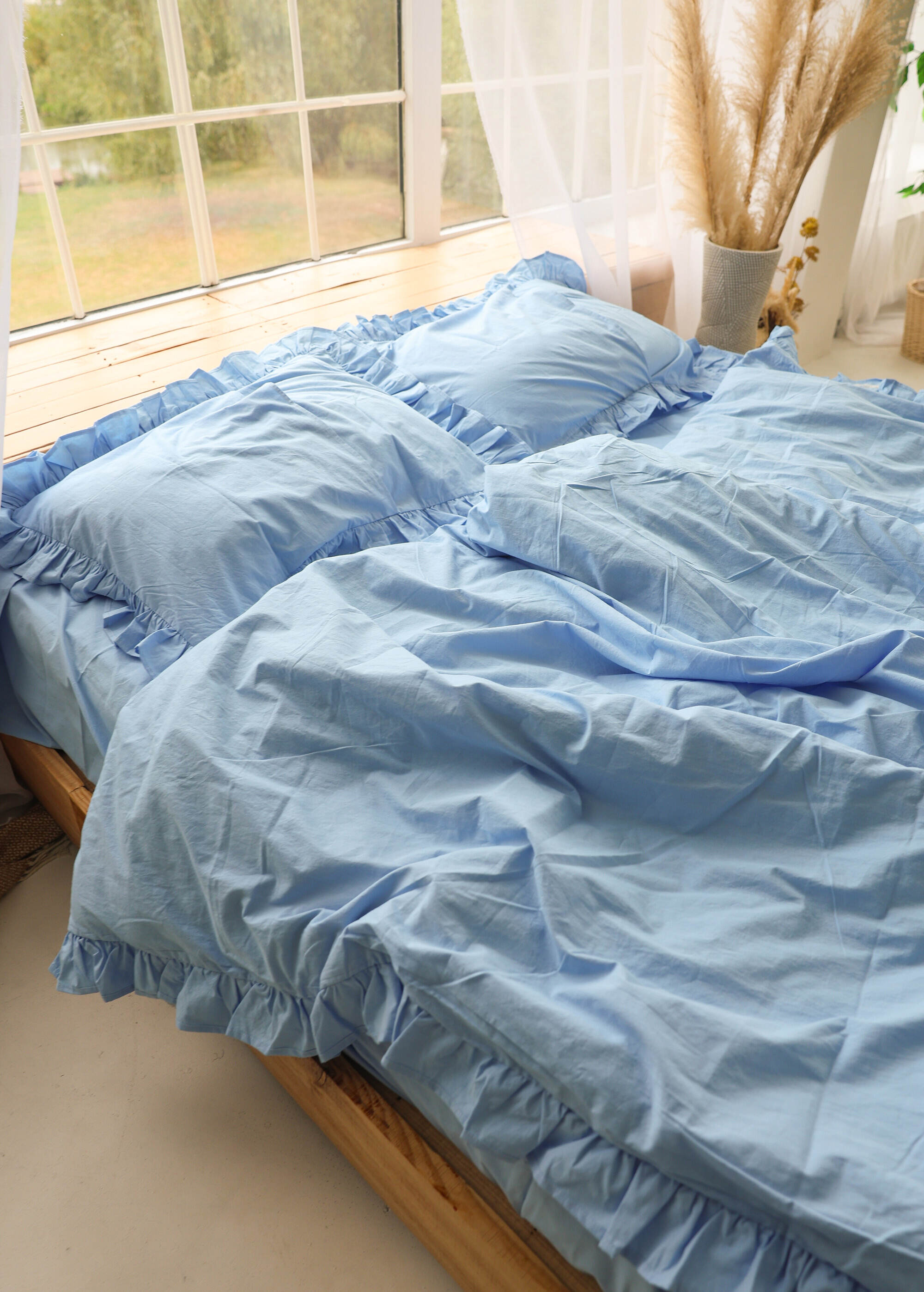 a bed with a blue comforter next to a window