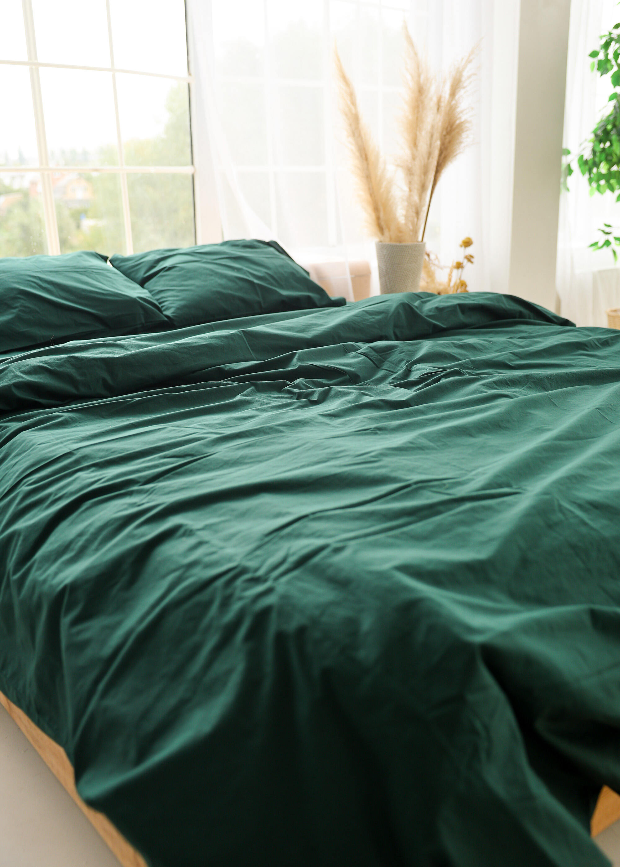 a bed with a green comforter next to a window